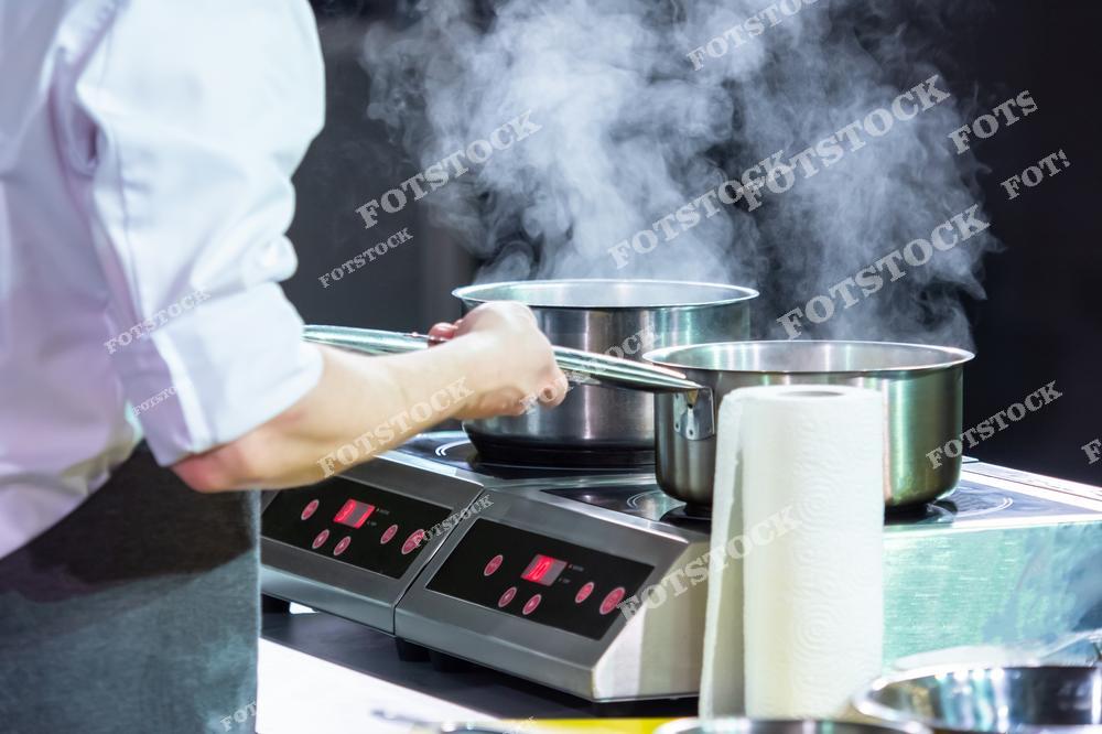 На изображении повар готовит блюдо в кастрюлях на индукционной плите. Пар поднимается из посуды, подчеркивая активный процесс тепловой обработки ингредиентов. Это рабочее место иллюстрирует профессиональный подход к приготовлению соусов и других блюд.